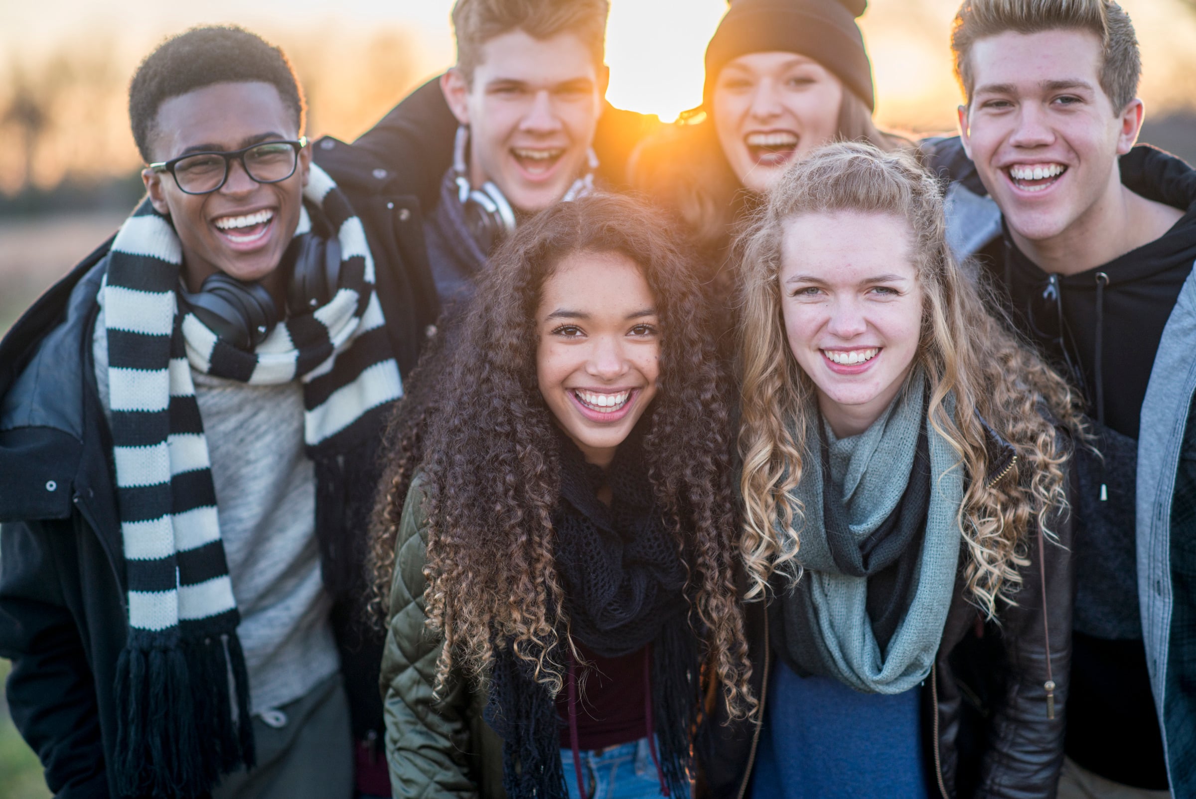A group of smiling teenagers outdoors at sunset